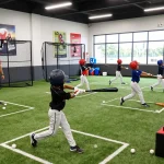 Young athletes training at hitclub indoor batting cage with coaches guiding swings.